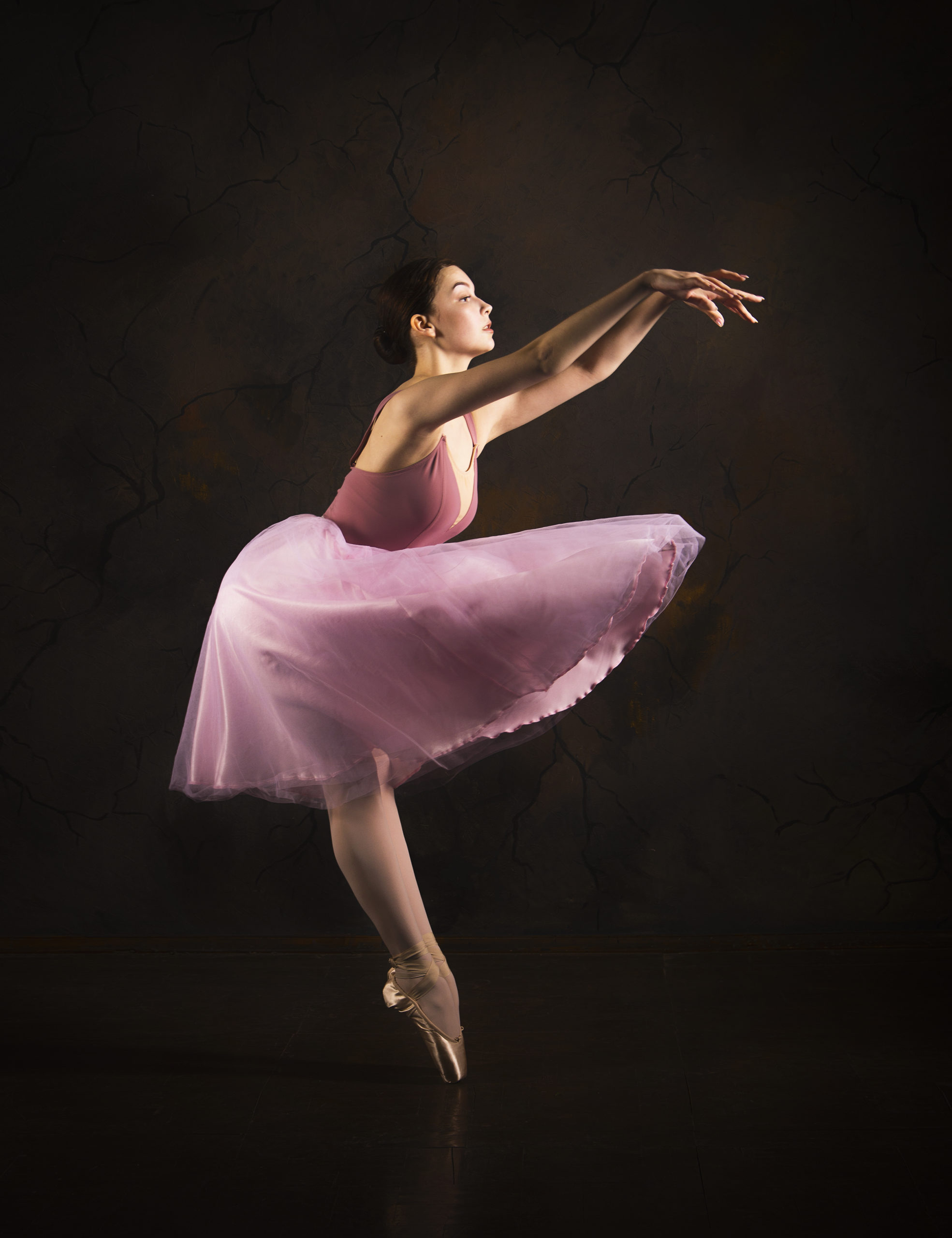A slender girl in a pink skirt and beige top dancing ballet.